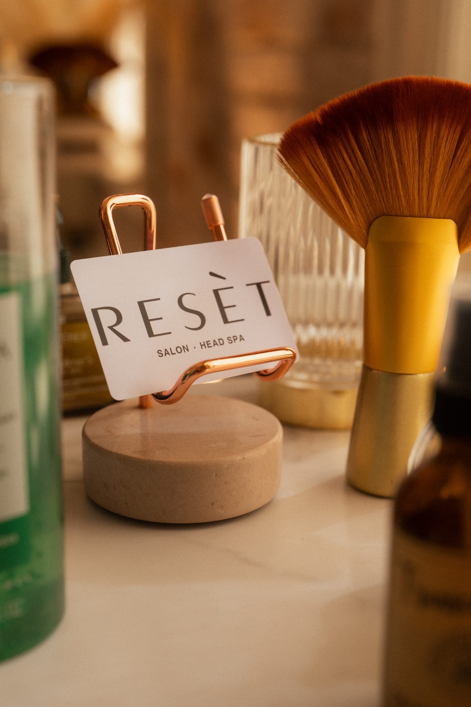 The Resèt Salon · Head Spa card on a stone stand beside brass brushes.