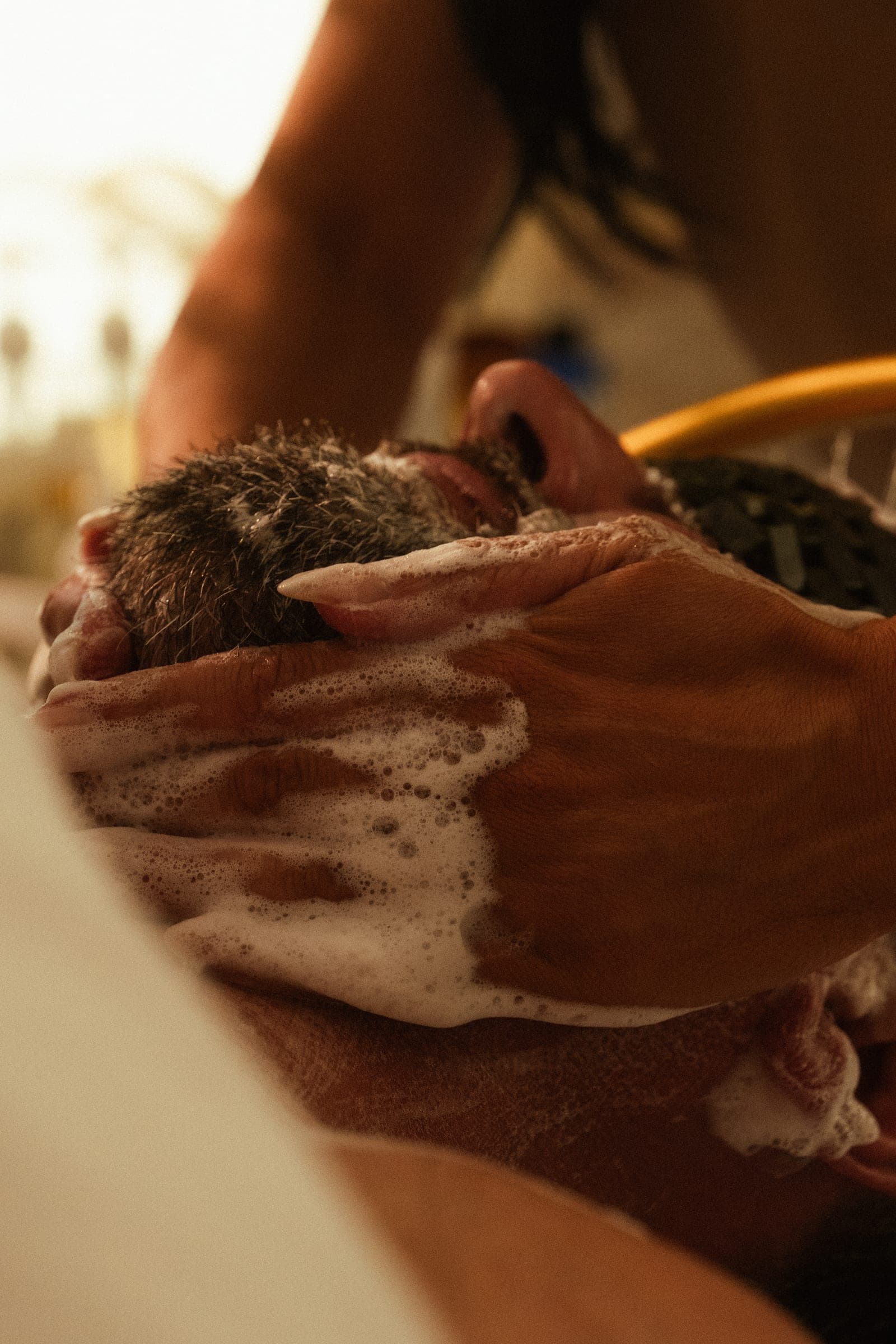 Hands working lather through a male guest's scalp during the Gentleman's Ritual.