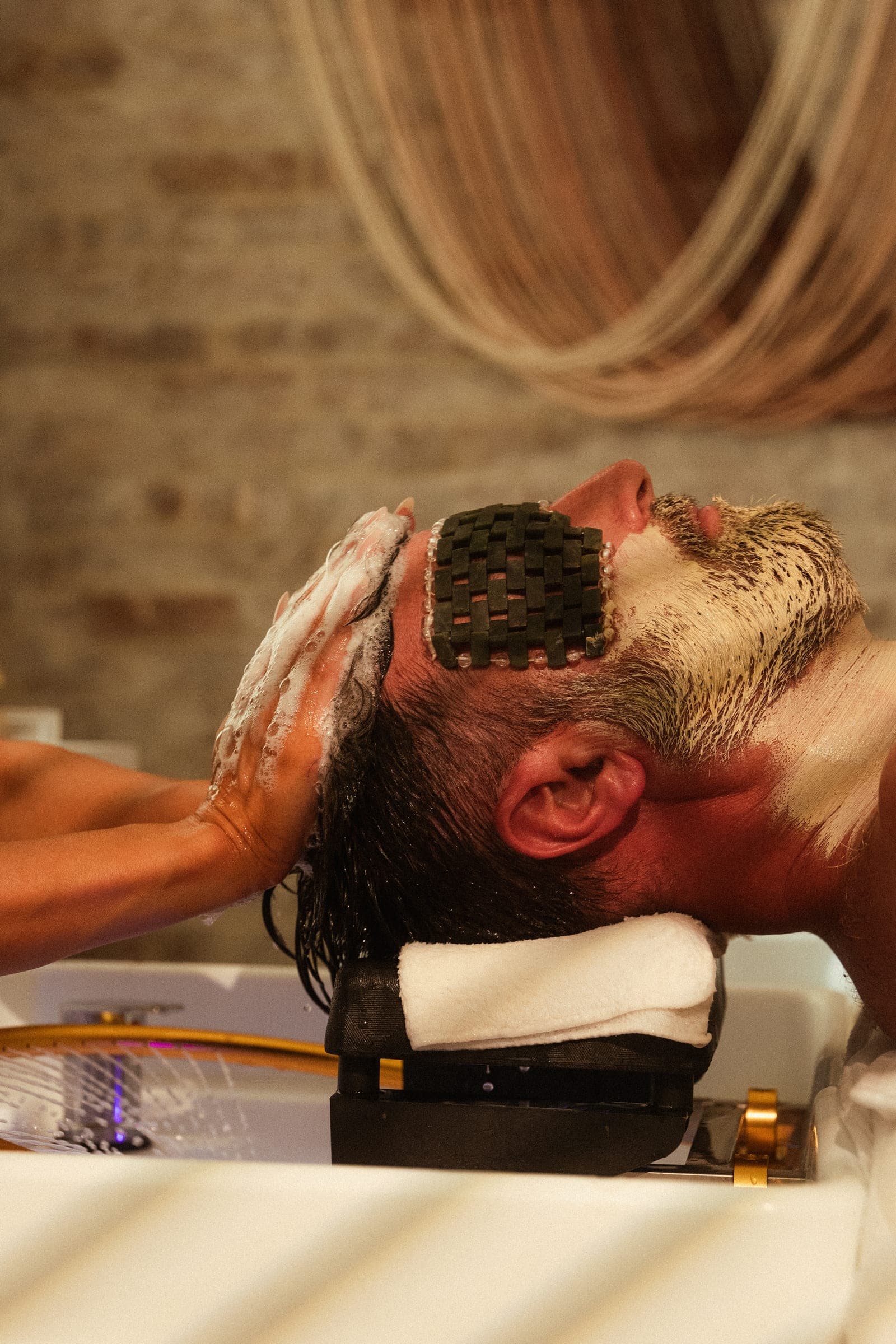 A male guest mid head spa ritual, eyes covered, reclined beneath the brass halo.