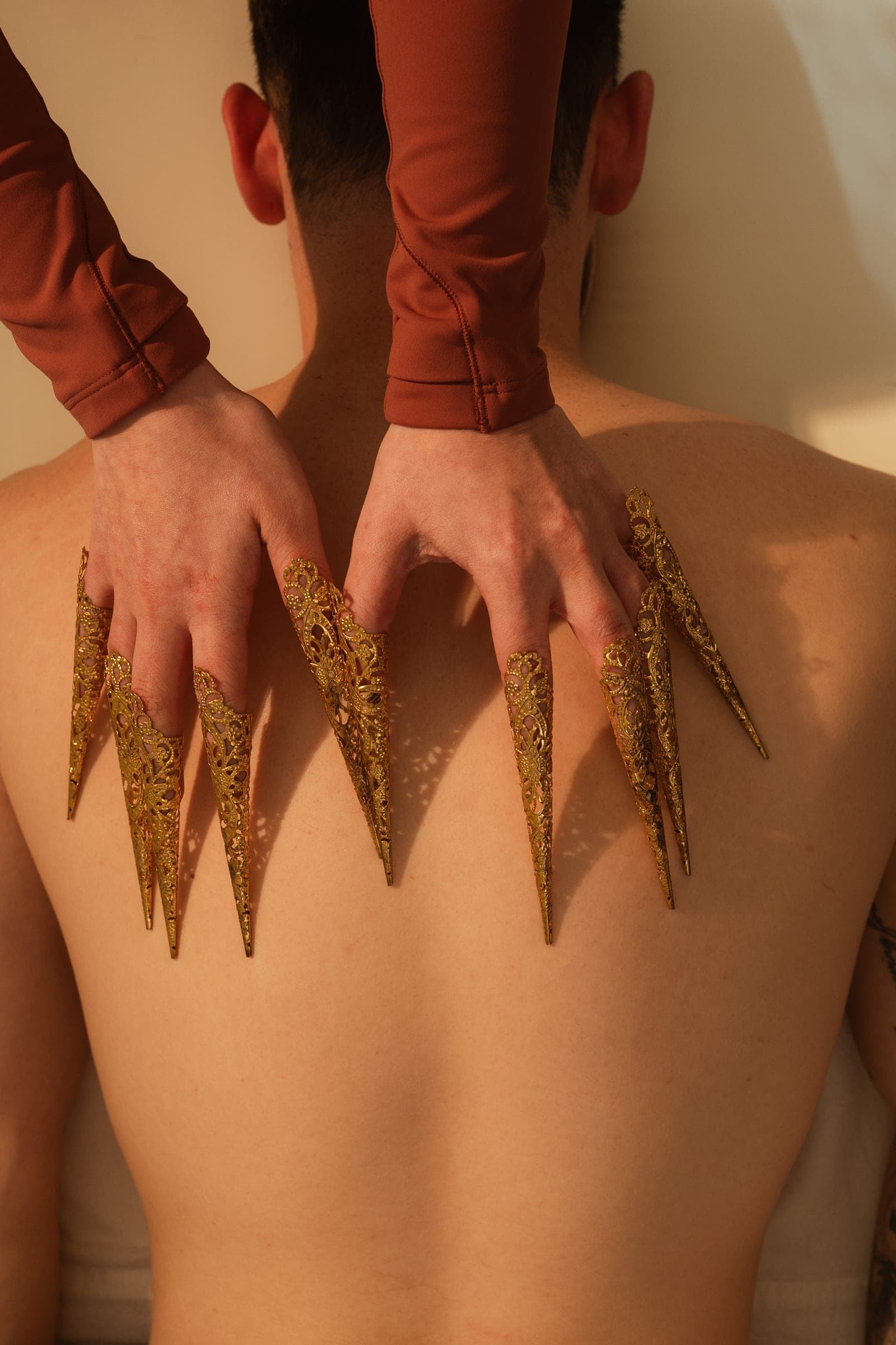 Both hands wearing brass scratch therapy claws over a guest's shoulders.