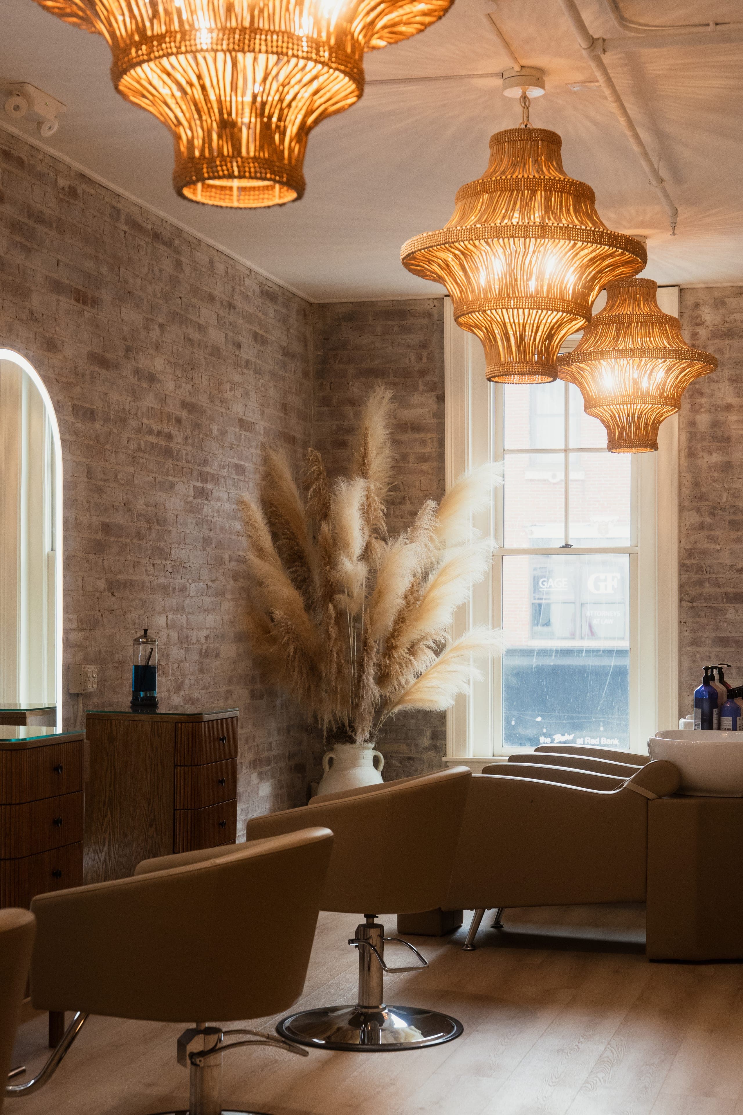 The Resèt salon floor in Red Bank — styling stations under woven pendant lights, exposed brick and dried pampas.